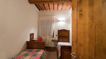 Un dormitorio pequeño con dos camas individuales, un armario de madera, una mesita y un radiador.