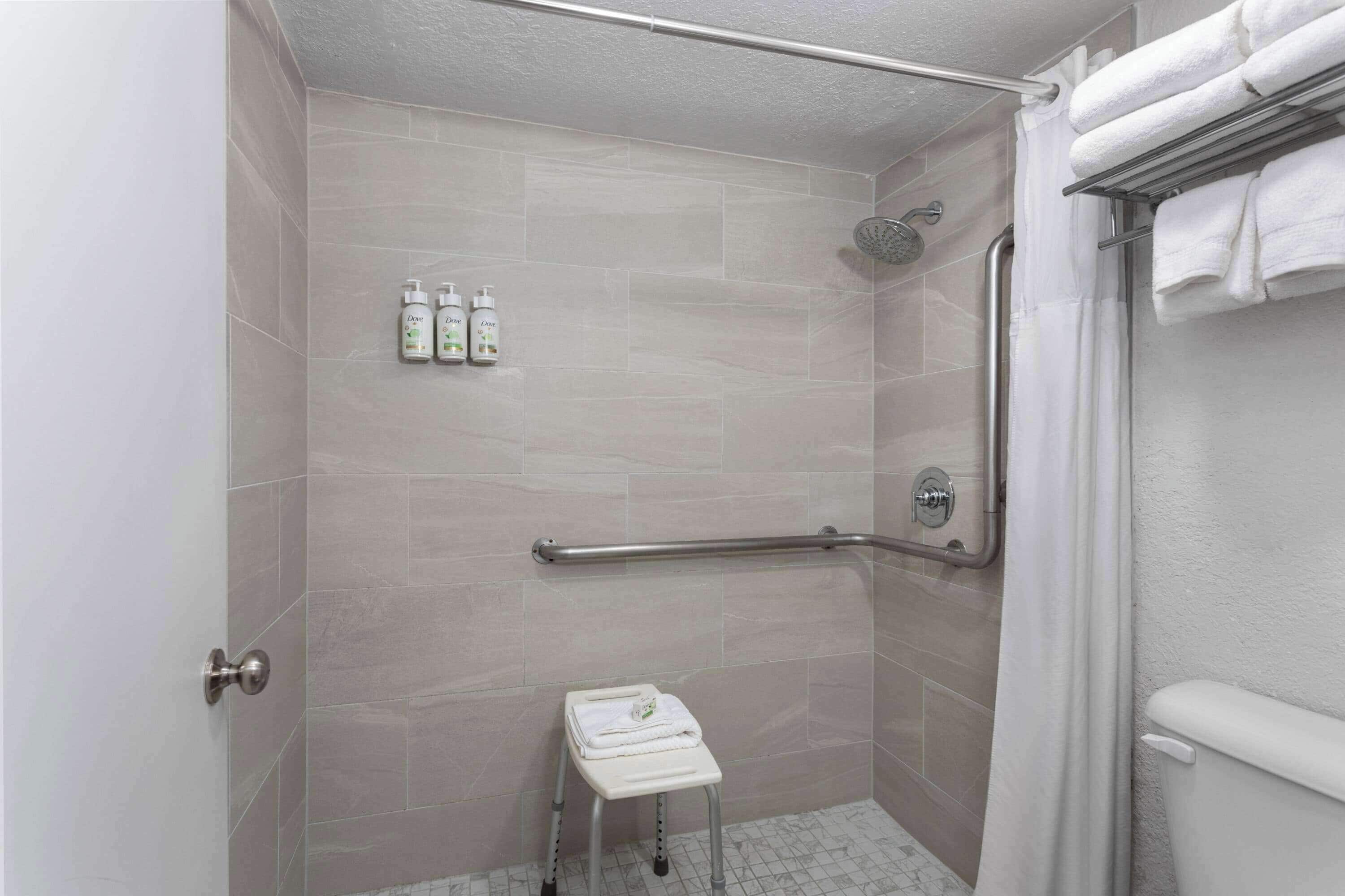 A shower area with a grab bar, a small step stool, and toiletries on the wall.