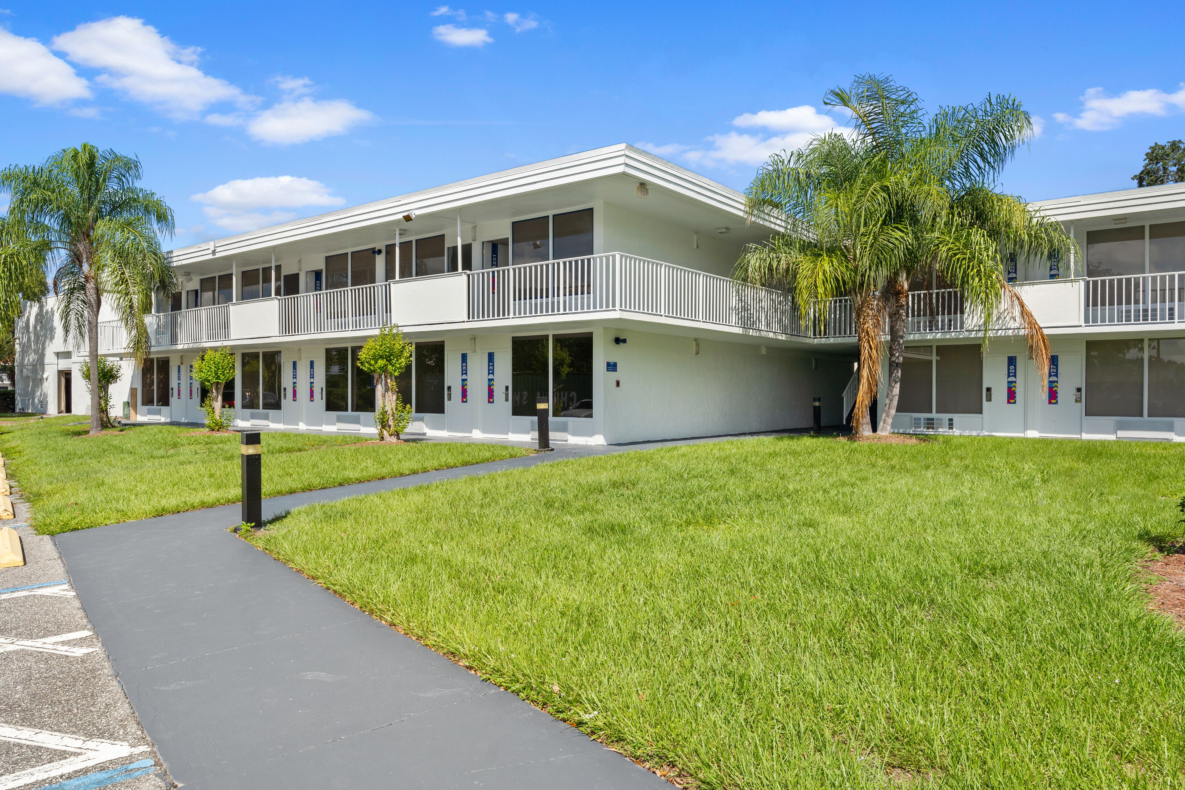 A two-story motel with a flat roof, a covered walkway, and a grassy lawn.