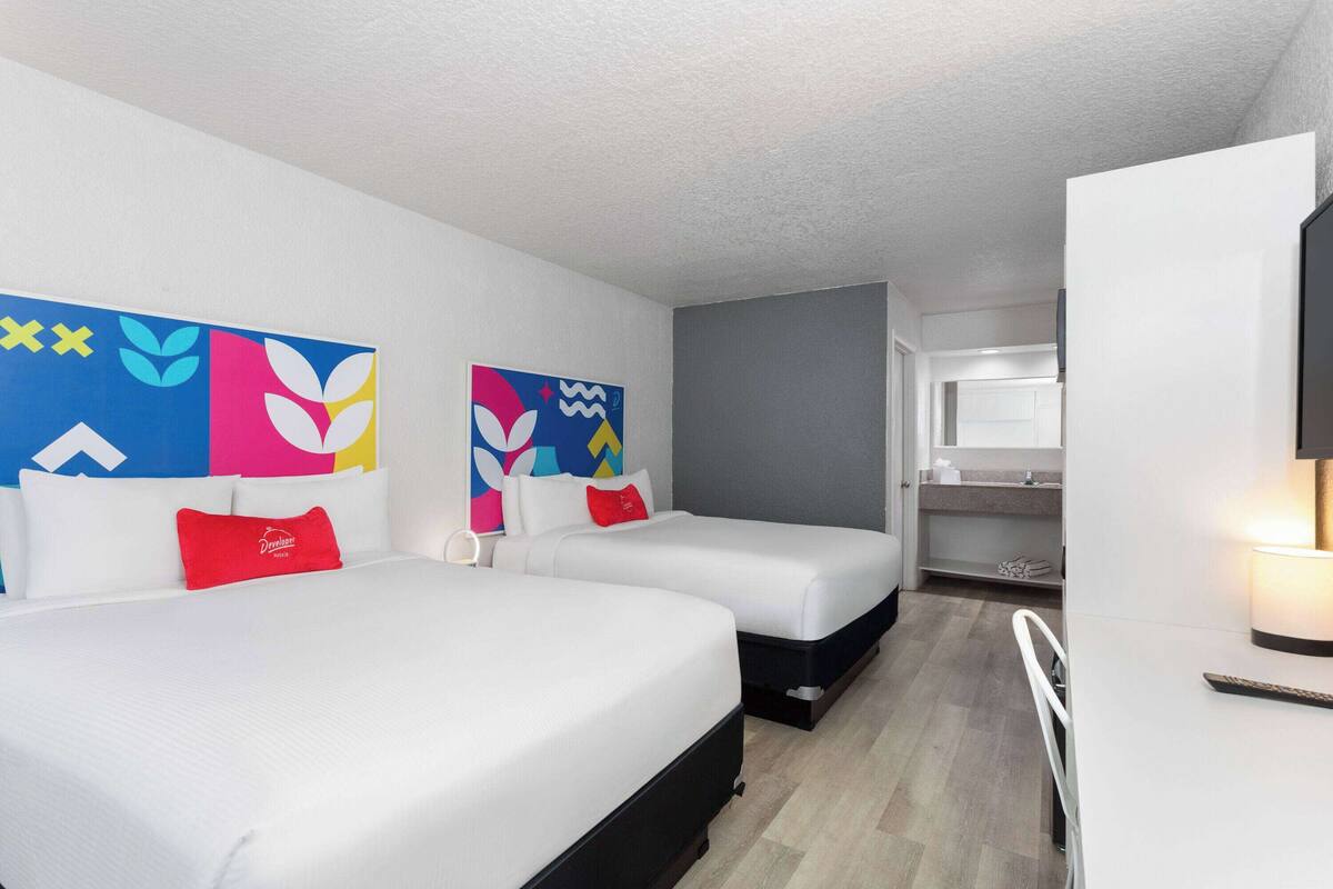 A hotel room with two beds, a desk, a chair, a TV, and a bathroom visible through an open door.