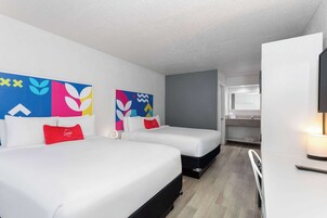 Une chambre d’hôtel avec deux lits, un bureau, une chaise, une télévision et une salle de bain visible à travers une porte ouverte.