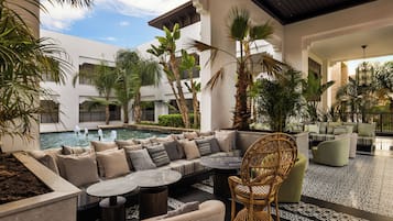 Zona de piscina con asientos, palmeras y vistas a un edificio con balcones.