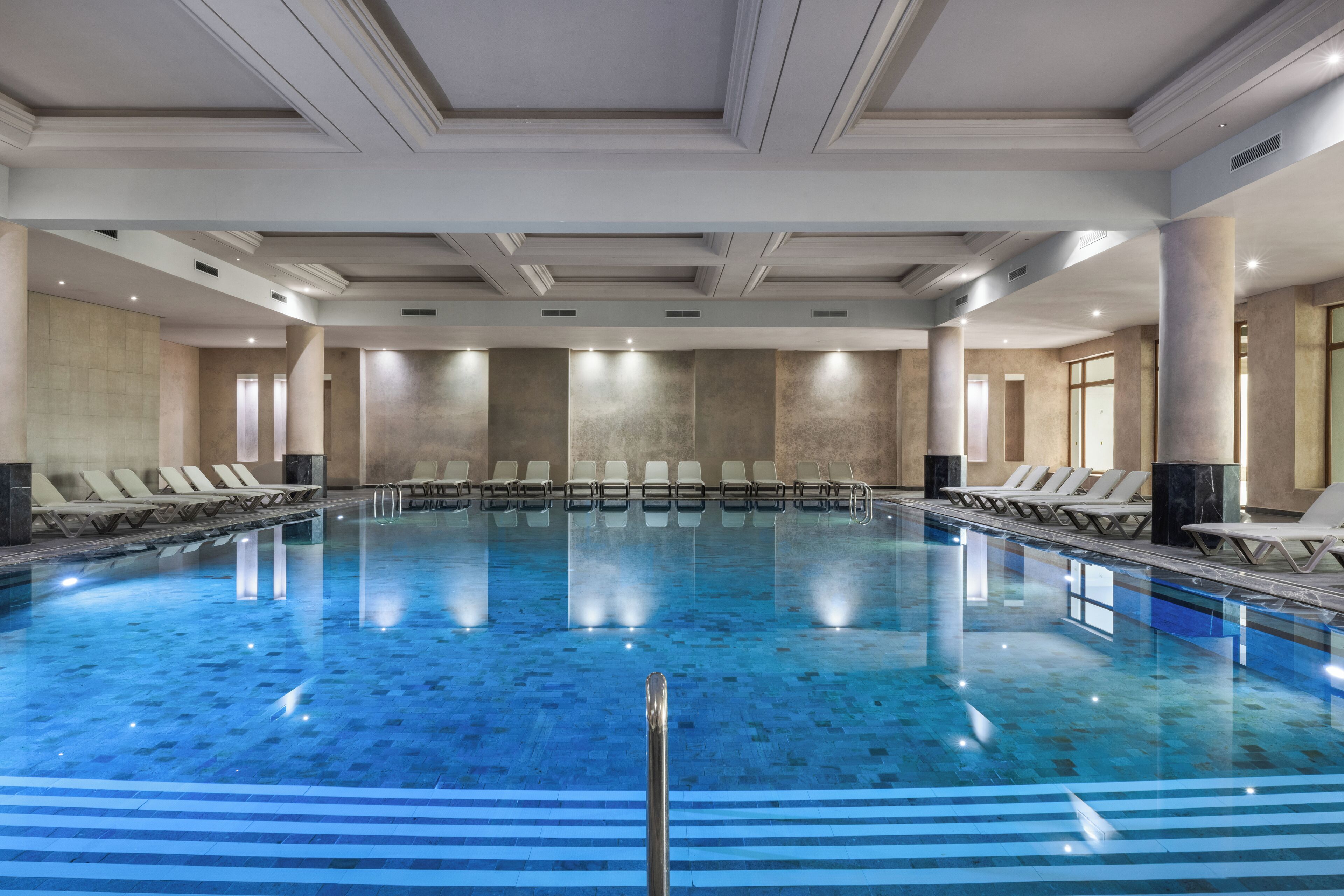 Une grande piscine intérieure dotée de chaises longues et d’un design moderne au niveau du plafond.