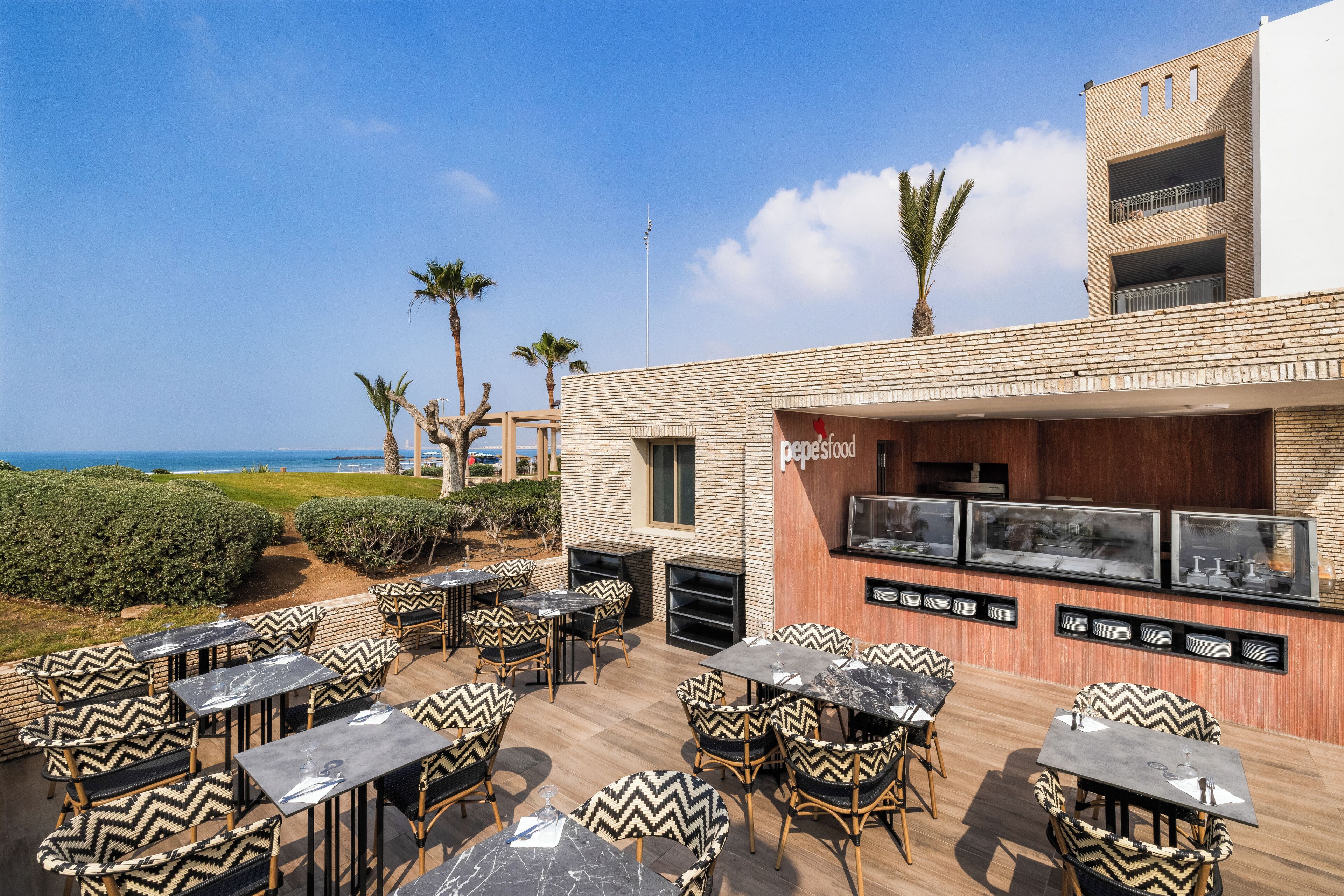An outdoor dining area with tables and chairs, a bar, and a view of the sea.
