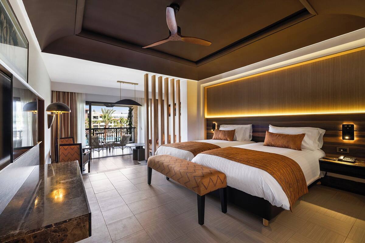A modern hotel room with a large bed, a desk, a balcony, and a ceiling fan.