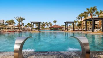 A swimming pool with two large metallic structures in the foreground, surrounded by lounge chairs and palm trees.