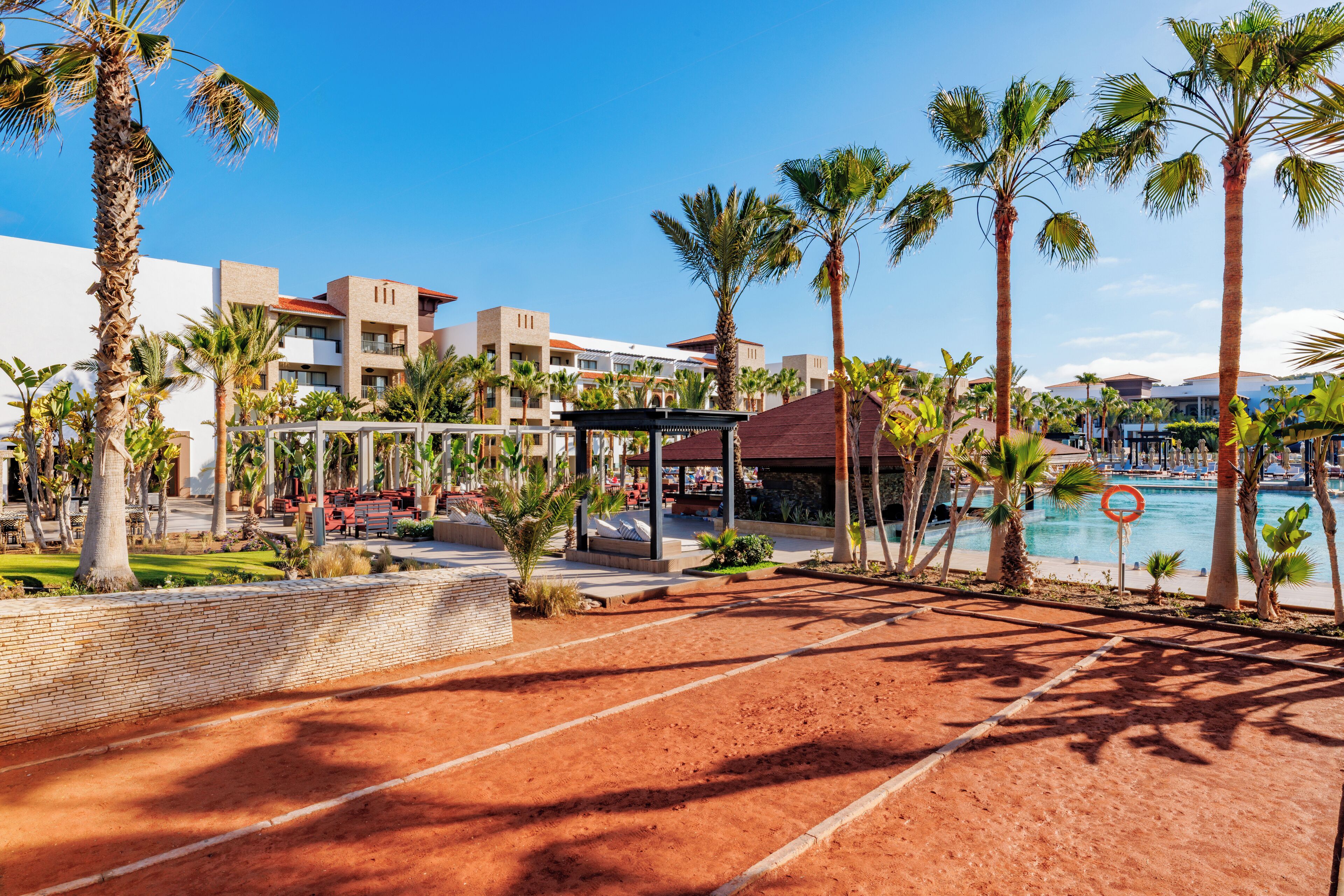 A resort with a pool, palm trees, and a covered seating area.