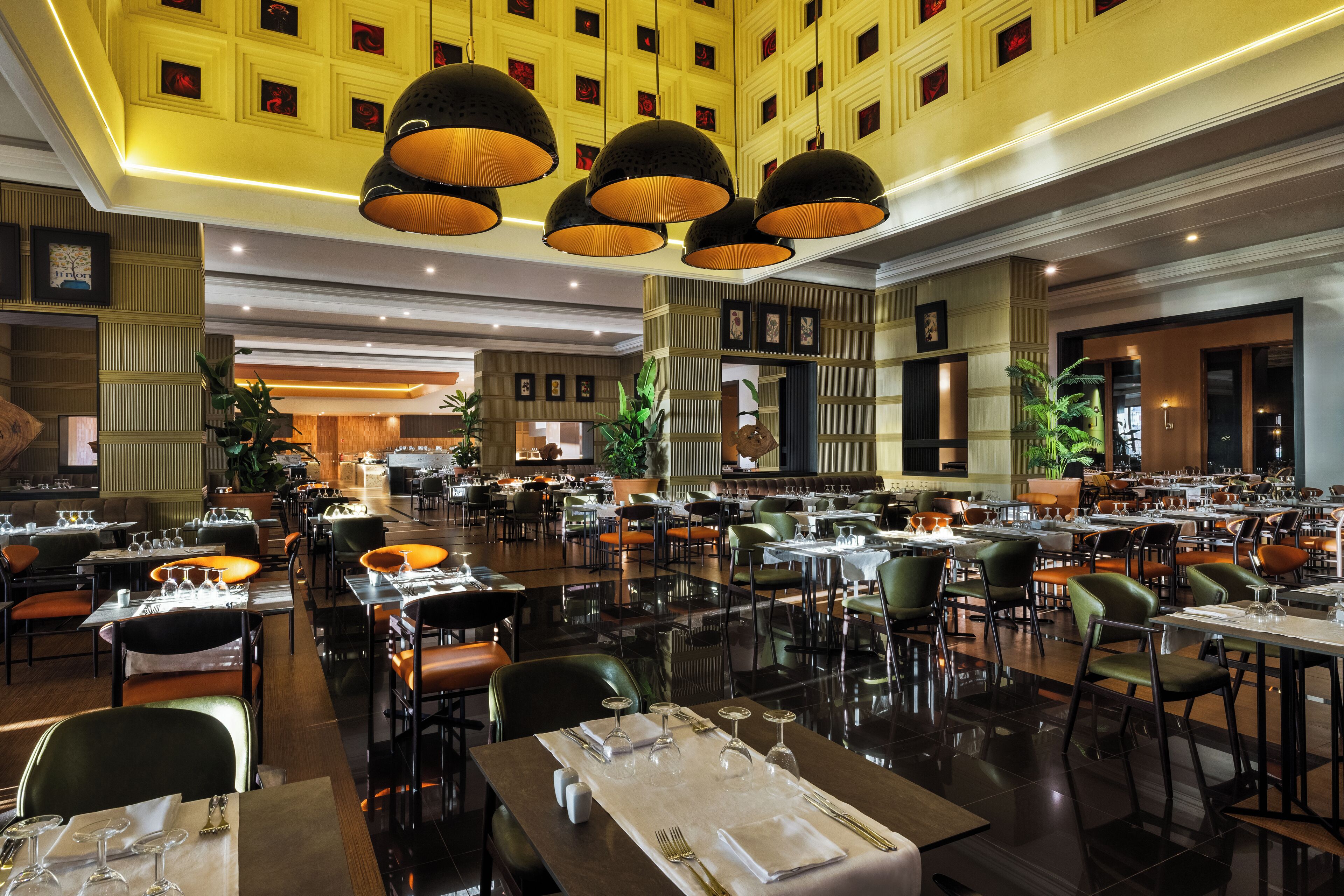 A spacious hotel dining area with multiple tables and chairs, large pendant lights, and a modern interior design.