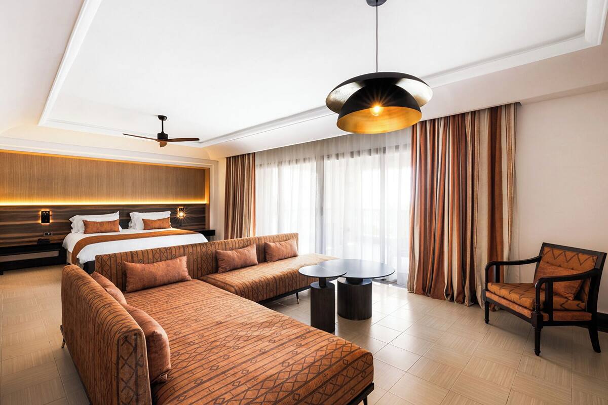 A modern hotel room with a large bed, a sofa, a dining table, and a chair.