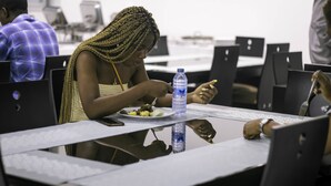 A person seated at a table with a laptop, a water bottle, and a plate of food. - Monarch Hotel (Accra)