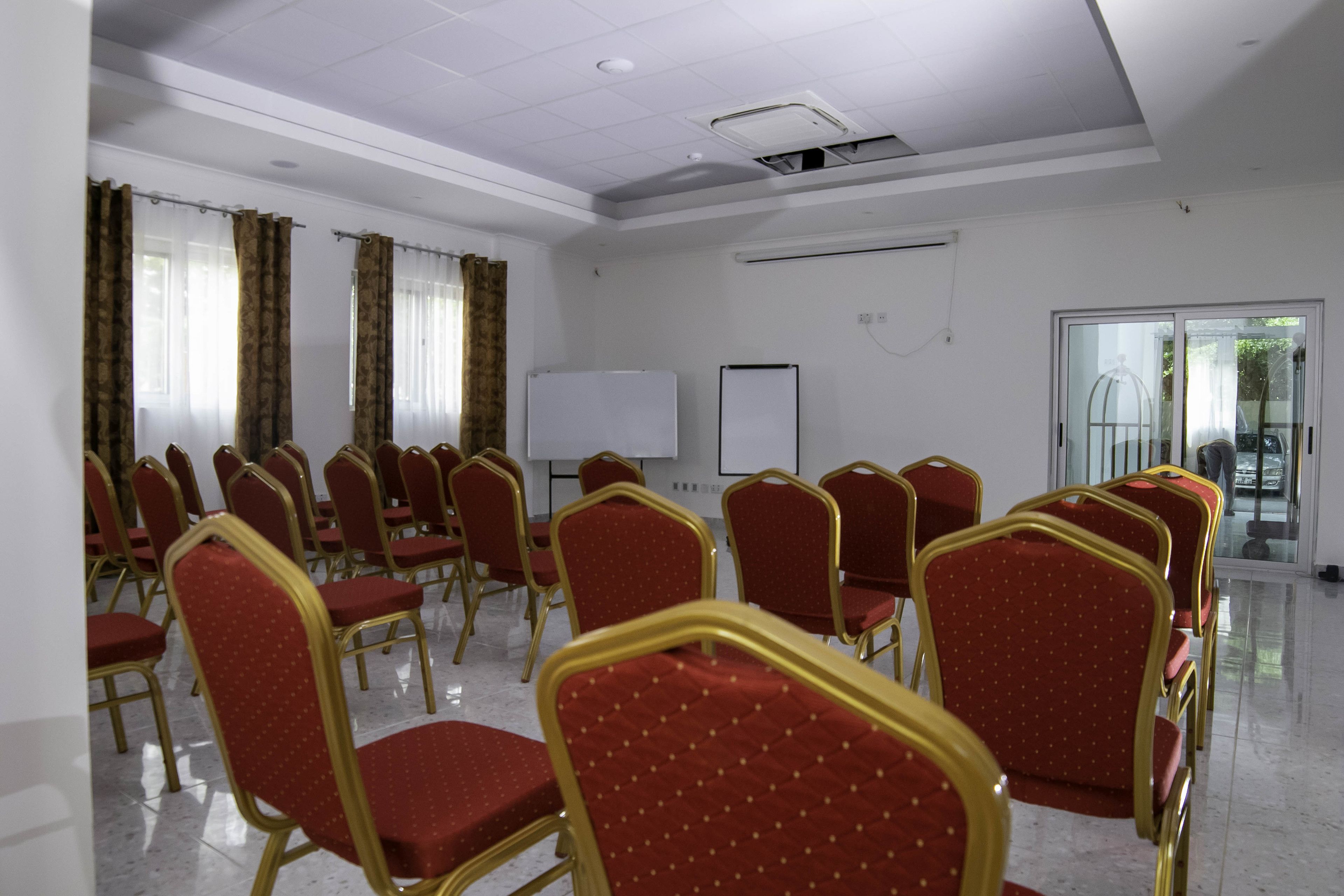 A conference room with rows of red chairs, a whiteboard, and a glass door leading outside.