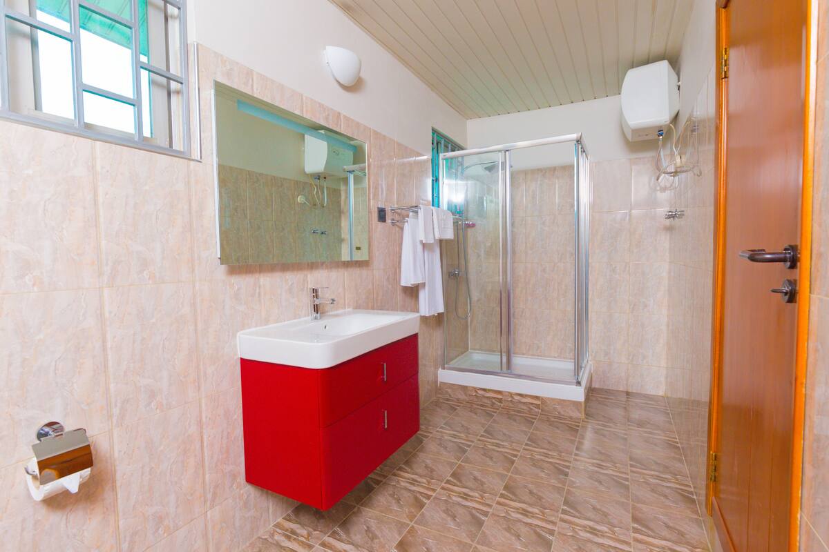 Ein modernes Badezimmer mit einer Glasdusche, einem roten Waschtisch und einem großen Spiegel.