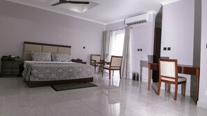 A modern bedroom with a bed, desk, chairs, and an air conditioning unit. - Monarch Hotel (Accra)