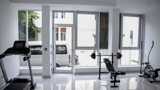 A gym with a treadmill, bench press, and elliptical machine. - Monarch Hotel (Accra)