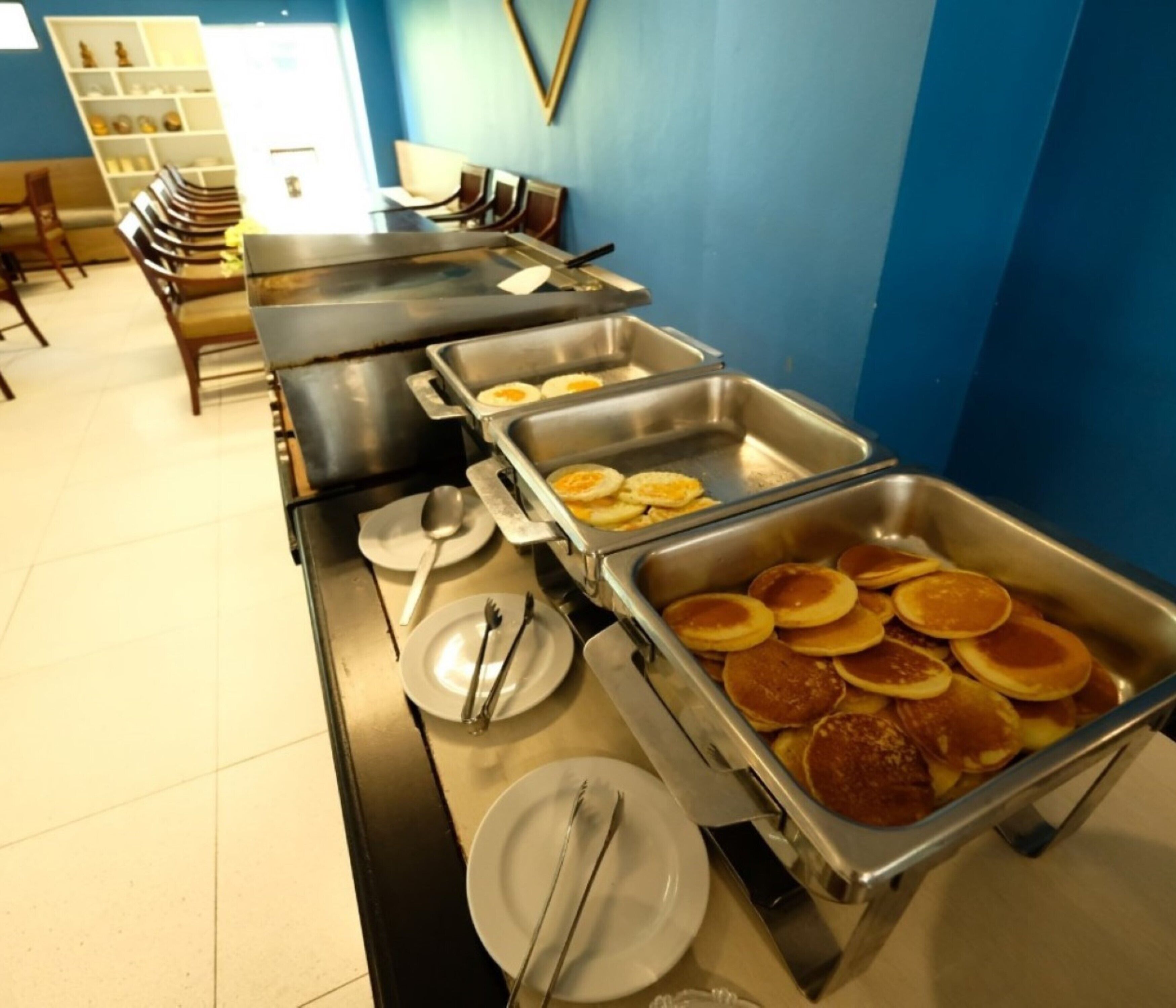 A buffet setup with multiple trays of pancakes and eggs.