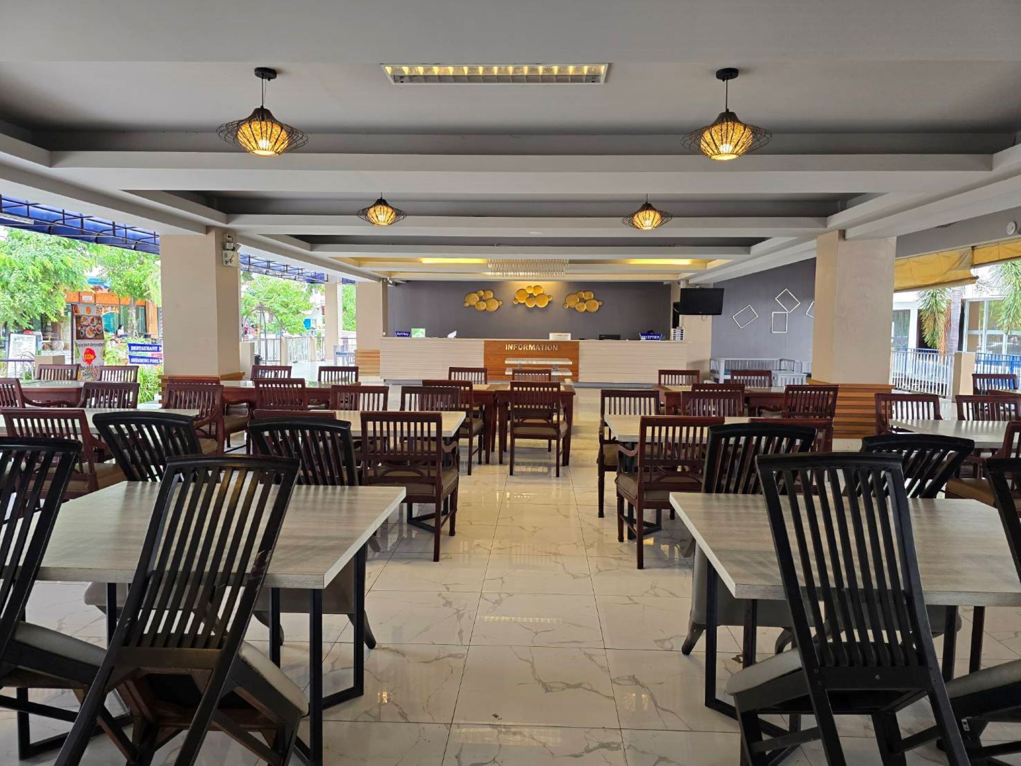 Un restaurante con varias mesas y sillas, un mostrador de recepción e iluminación decorativa.