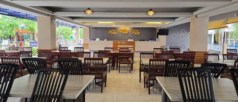 Un restaurante con varias mesas y sillas, un mostrador de recepción e iluminación decorativa.