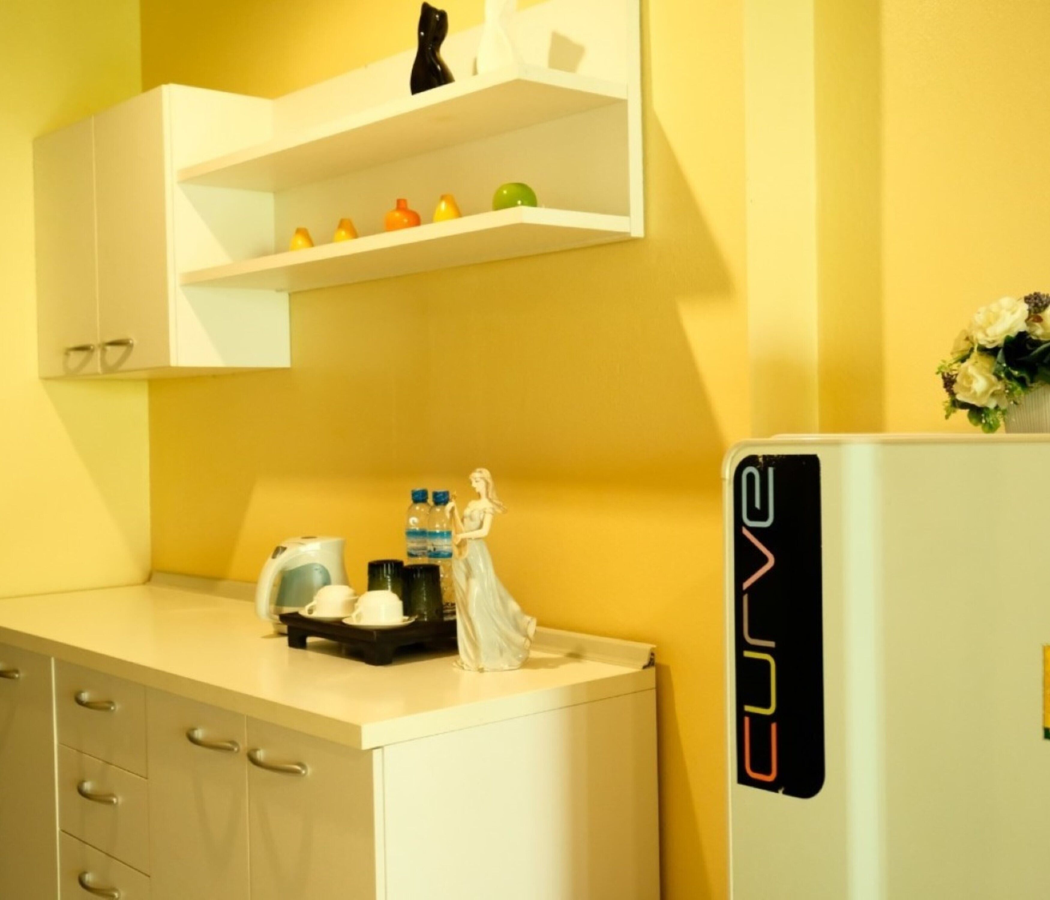 A kitchen with a white countertop, a white refrigerator, and a shelf with various items.
