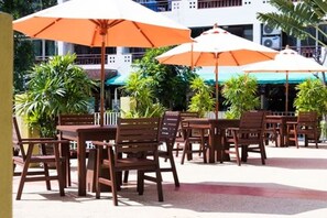 Un espace extérieur aménagé avec des tables et des chaises en bois, des parasols orange et des plantes en pot.