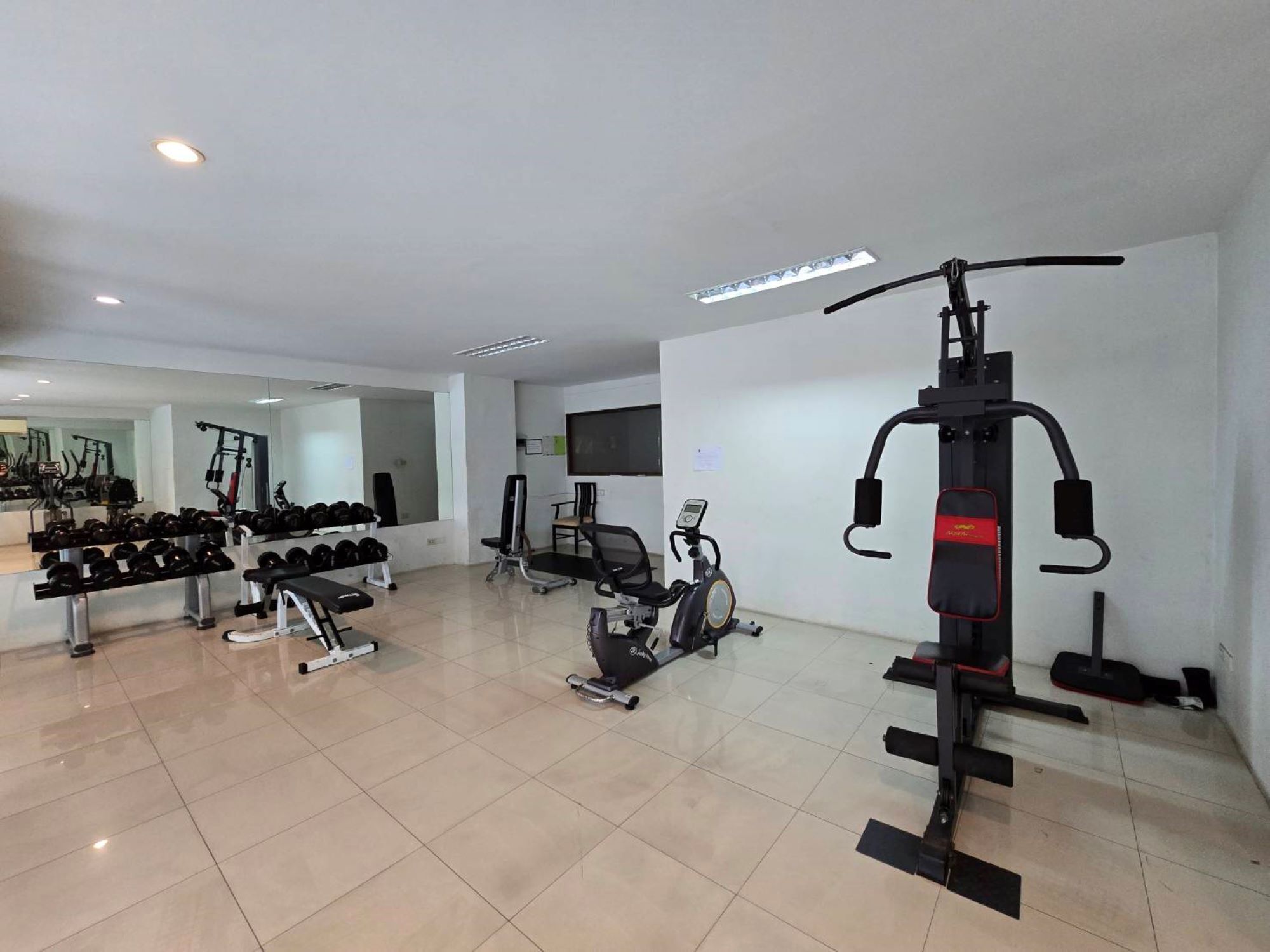 A gym with exercise equipment, weight benches, and dumbbells.