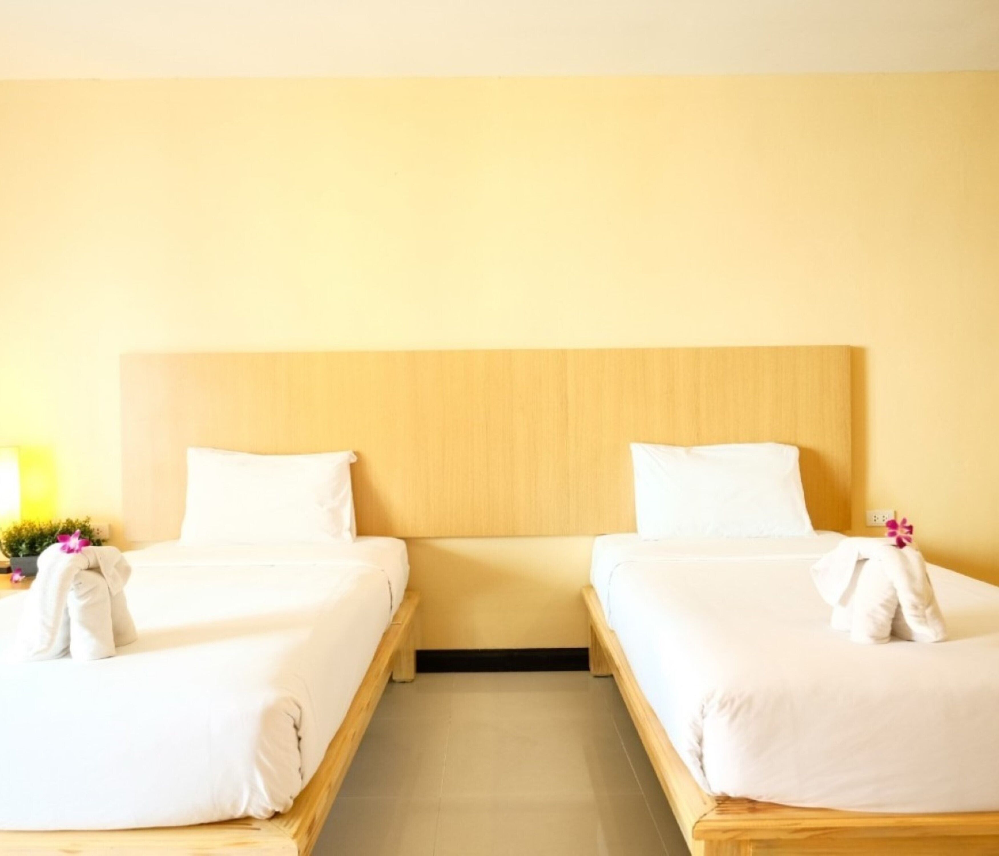 A hotel room with two single beds, wooden headboards, and a small bedside table with a lamp.