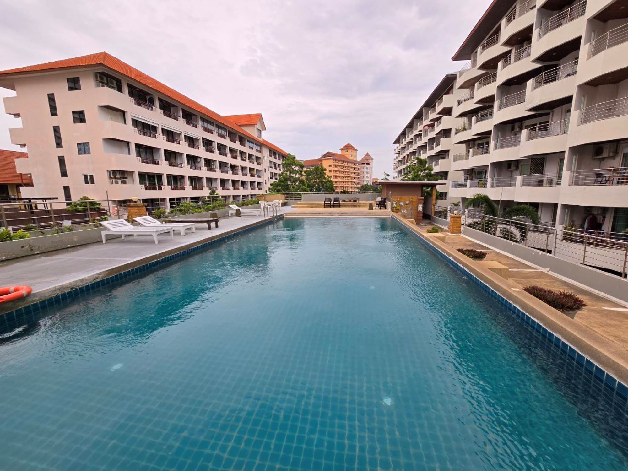 Piscina com espreguiçadeiras e um pequeno pavilhão, cercada por edifícios com varandas.