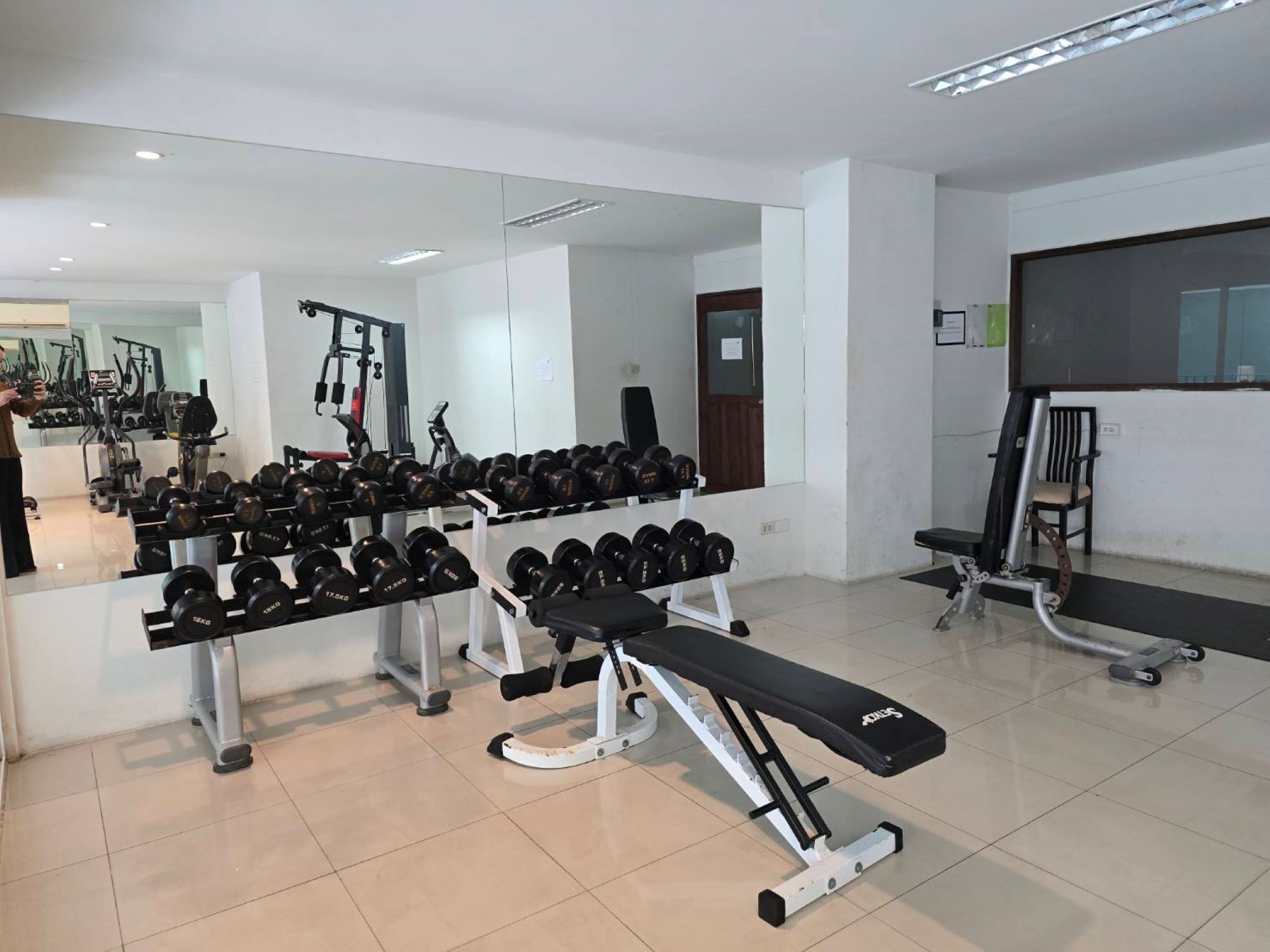Ein Fitnessstudio mit unterschiedlichen Trainingsgeräten, darunter Kurzhanteln, Bänke und Kraftgeräte.