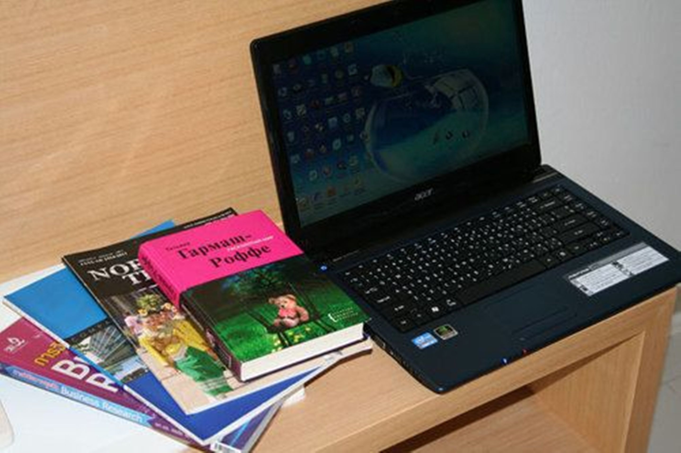 A laptop on a wooden desk with several books, including one titled "Capyambú."