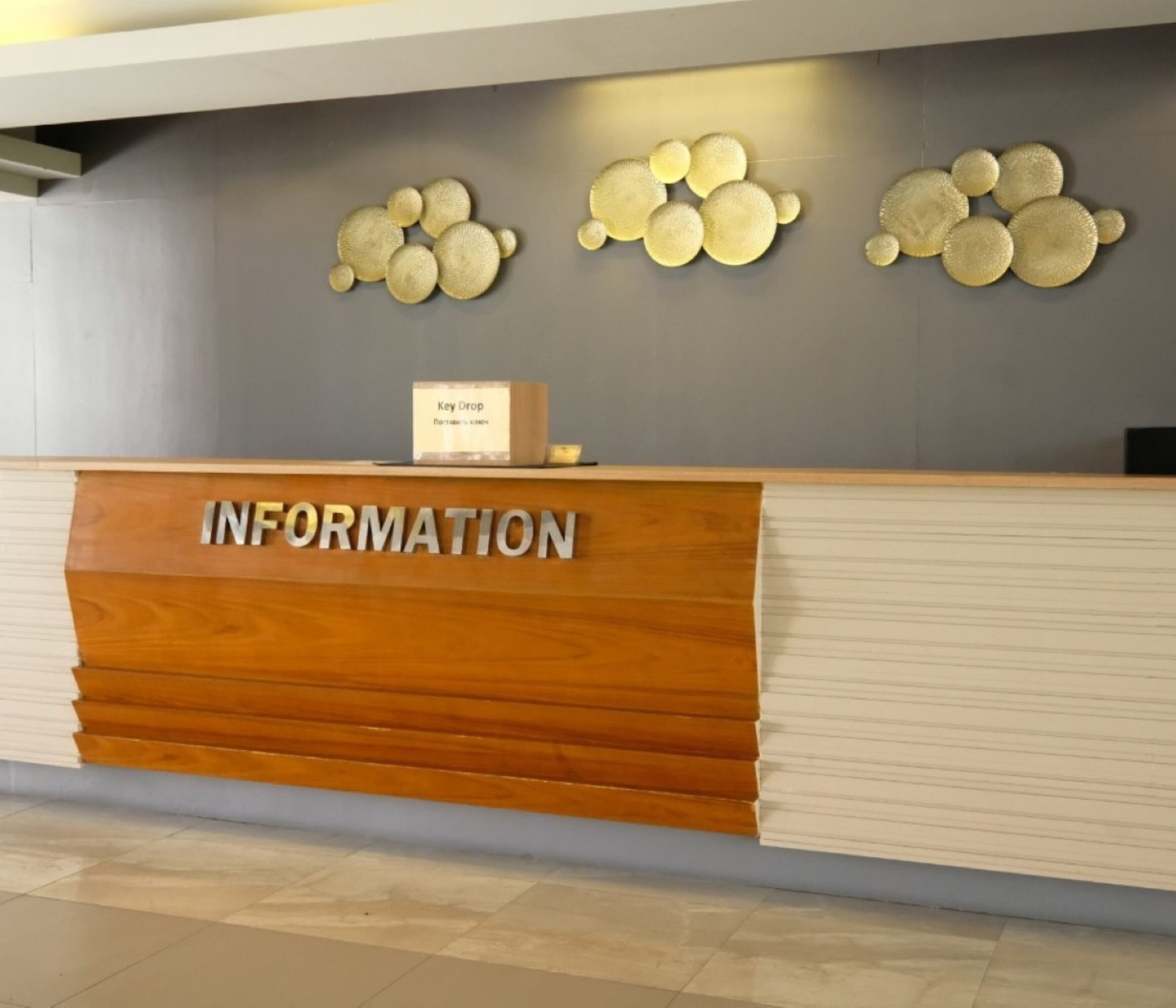 A reception desk with a wooden finish and the word "INFORMATION" on it. There are decorative wall pieces above the desk.