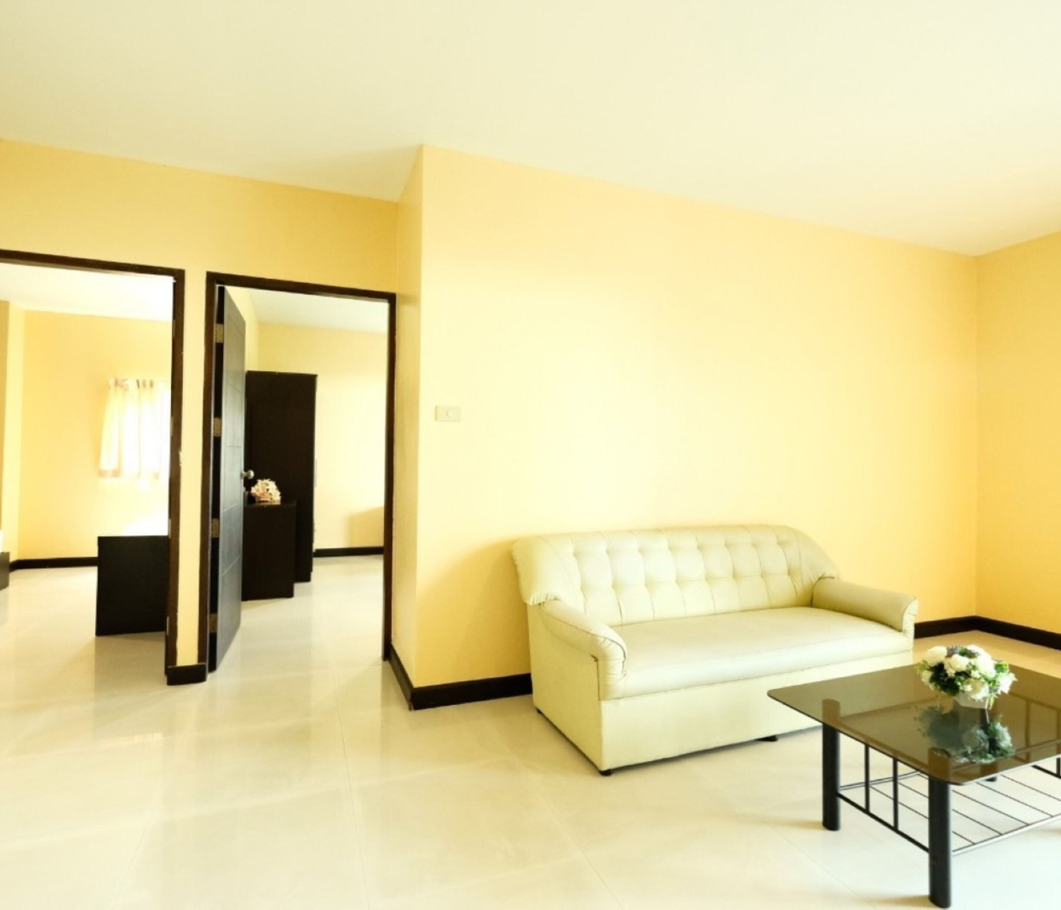 Una habitación con un sofá blanco, una mesa de centro de vidrio y un espejo que refleja una puerta y una ventana con cortinas.