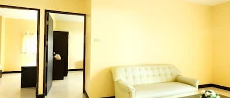 Una habitación con un sofá blanco, una mesa de centro de vidrio y un espejo que refleja una puerta y una ventana con cortinas.