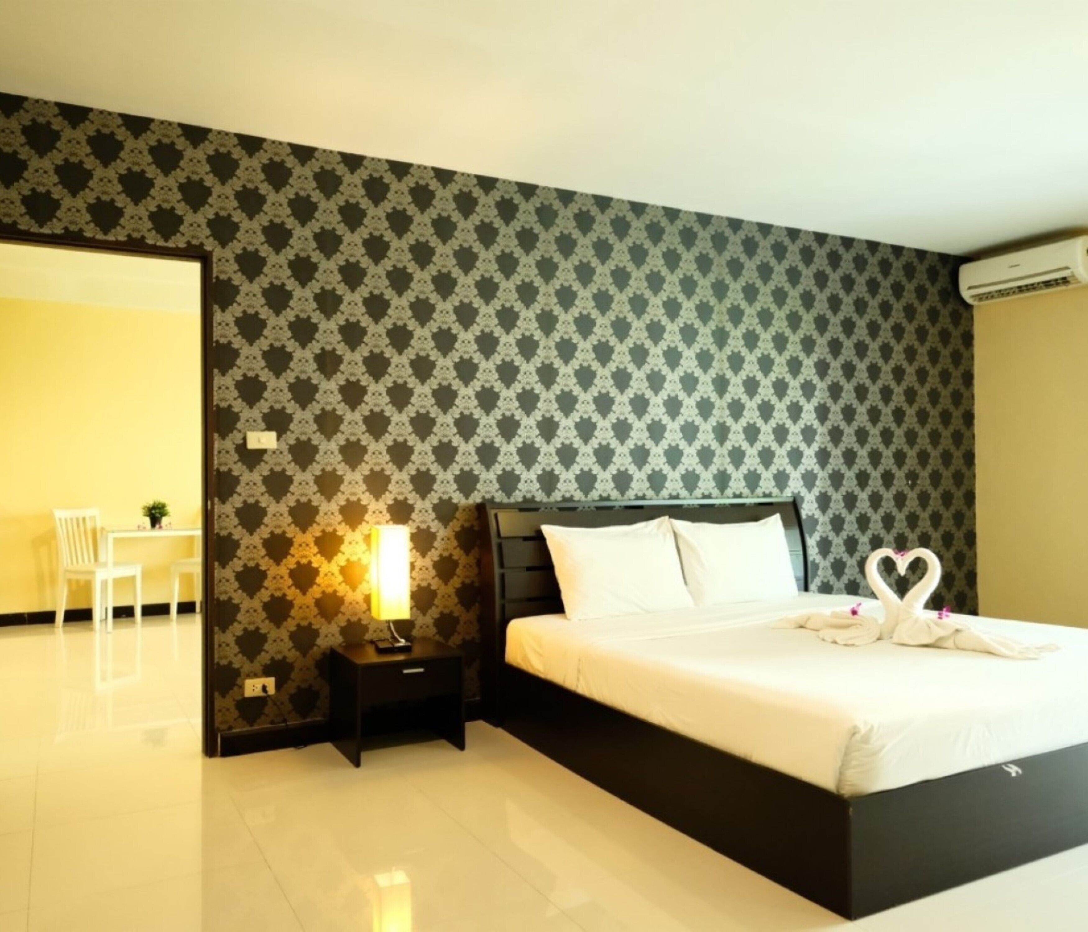 Una habitación de hotel con papel tapiz estampado, una cama con ropa de cama blanca, una mesita de noche con una lámpara y una silla en la esquina.