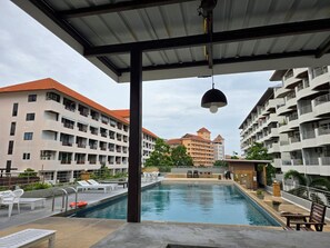 Une piscine dotée de chaises longues et d’un espace abrité, entourée d’immeubles à plusieurs étages avec des balcons.