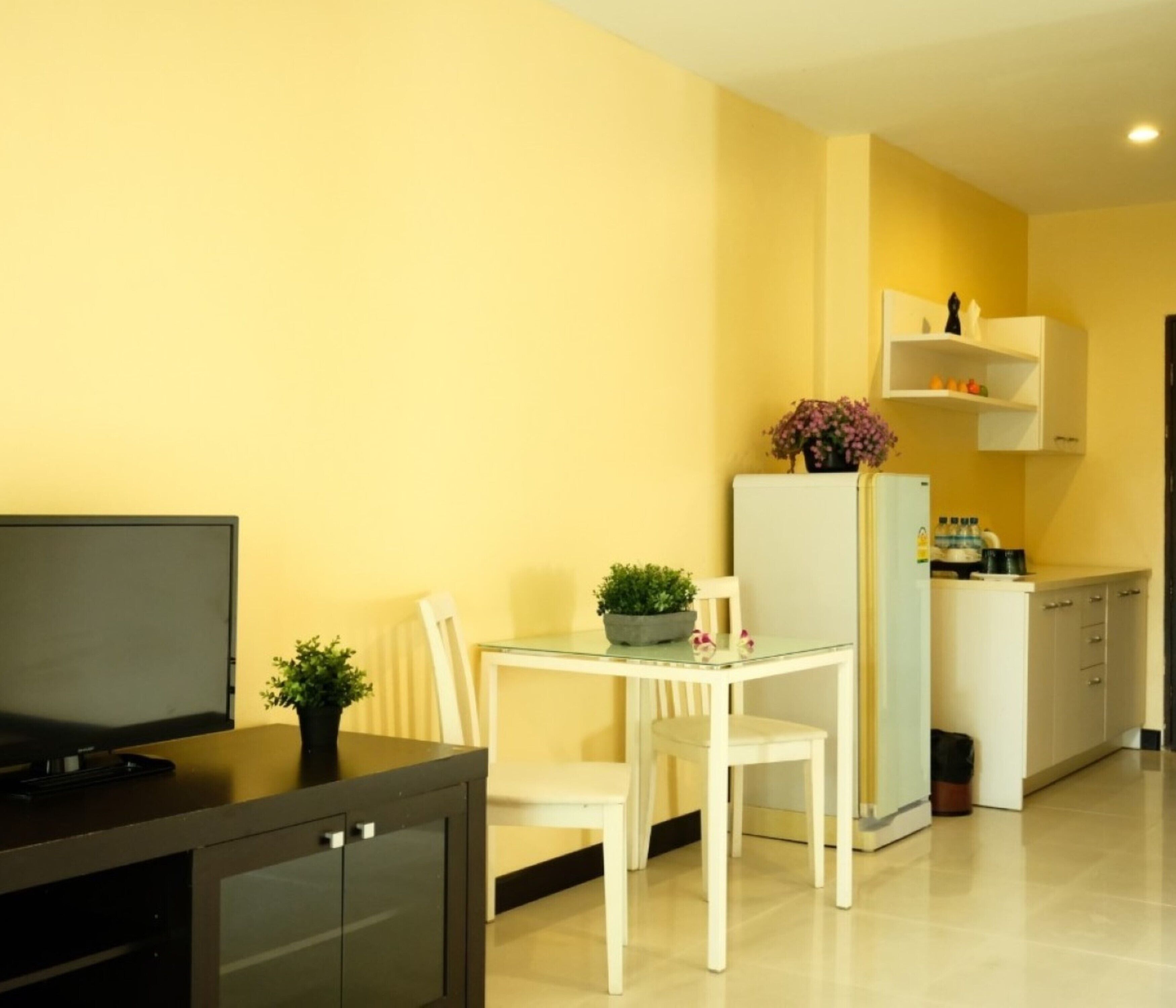 Een compacte keuken met een koelkast, een eettafel met stoelen en een tv op een kast.