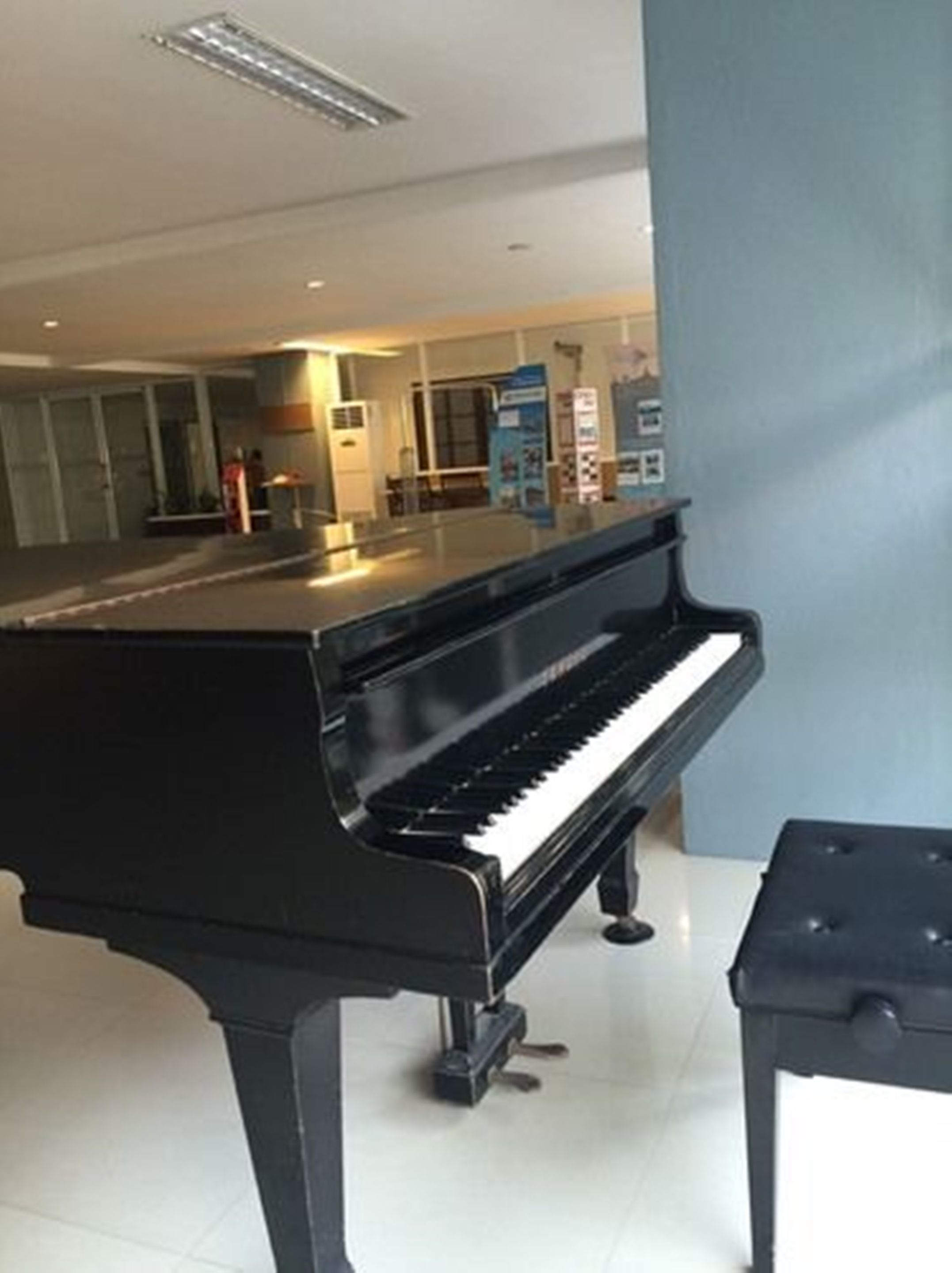 A black grand piano in a modern hotel lobby with a glass partition and a reception desk.