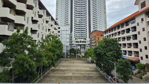 Un immeuble de grande hauteur doté de nombreux balcons, entouré d’autres immeubles et d’arbres.