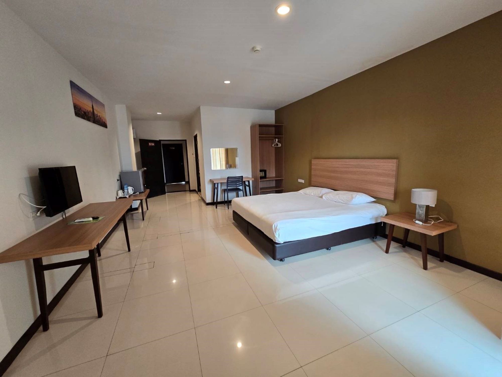 A hotel room with a bed, a desk, a chair, a TV, and a small table with a lamp.