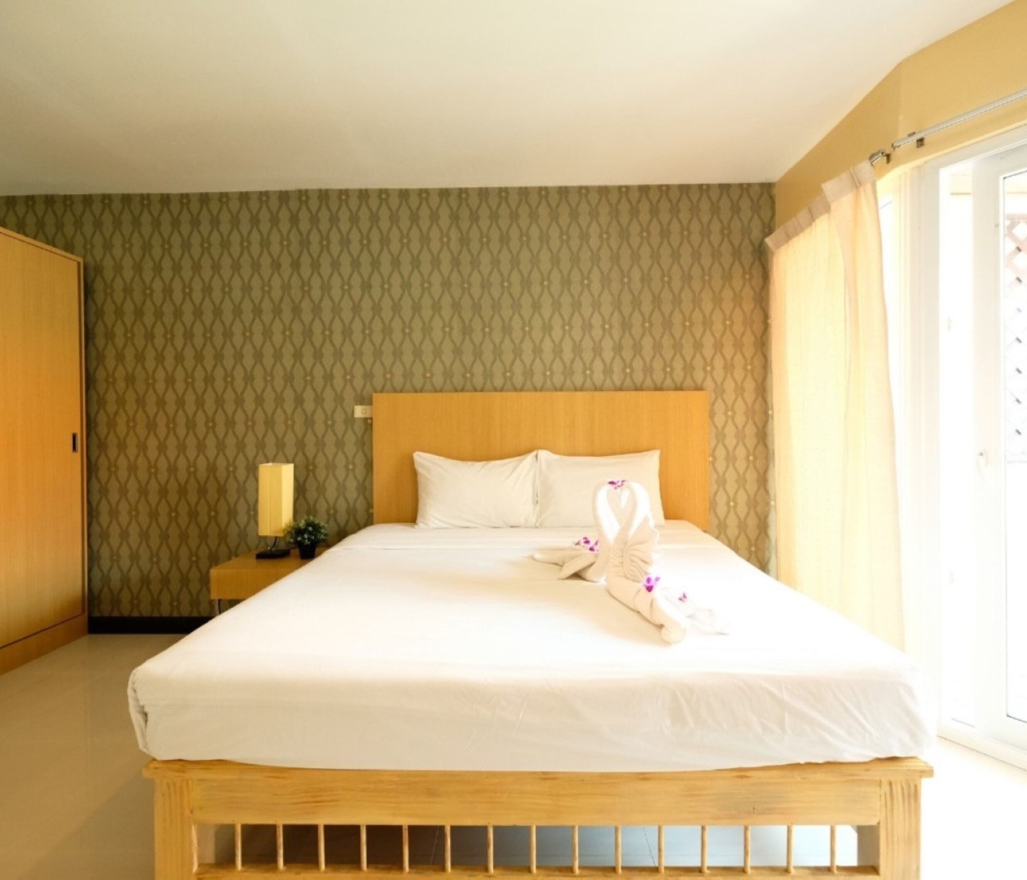 A neatly made bed with white linens and a wooden headboard, a bedside lamp, and a patterned wallpaper.