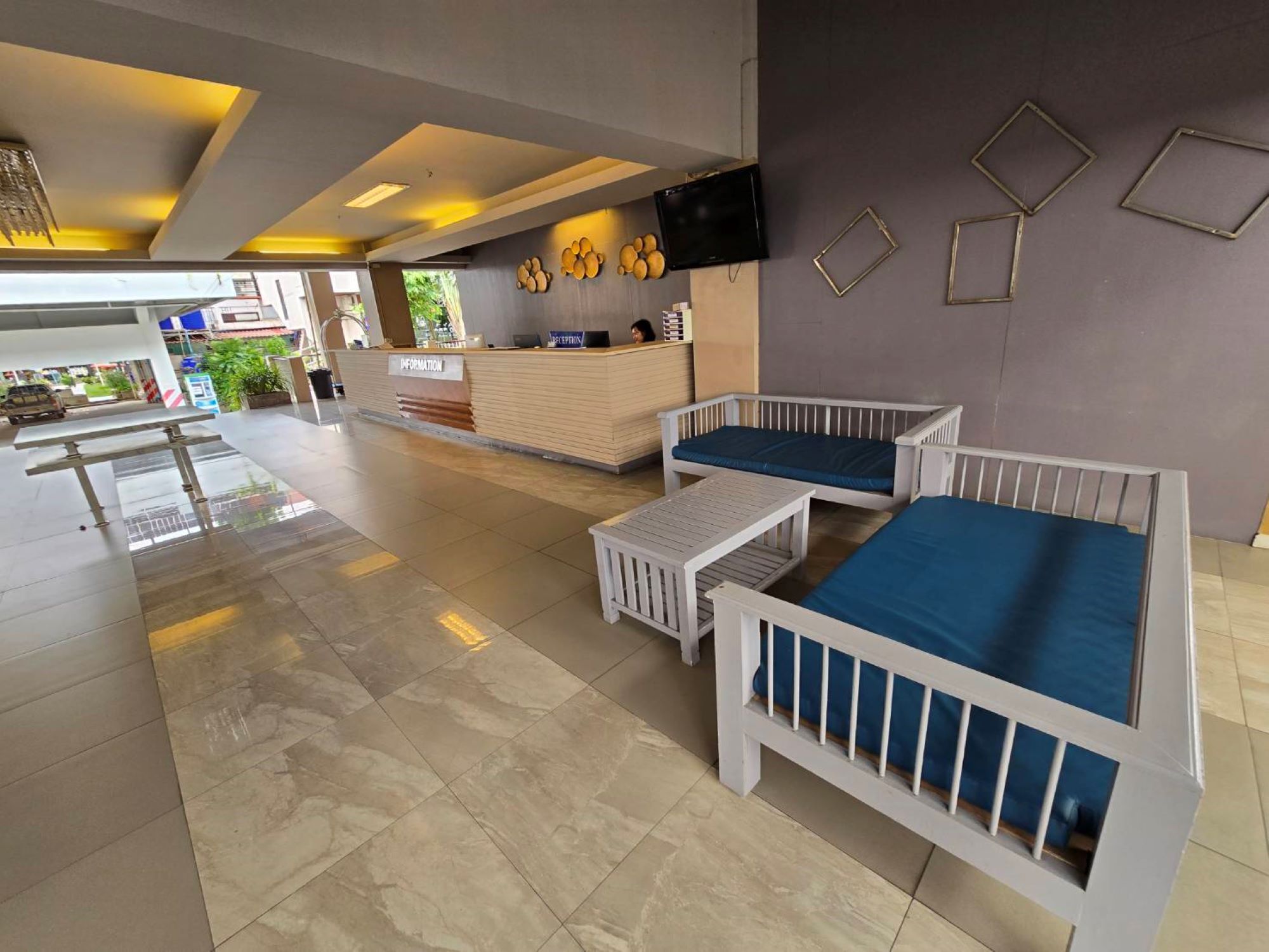 A hotel lobby with a reception desk, seating area, and a flat-screen TV on the wall.