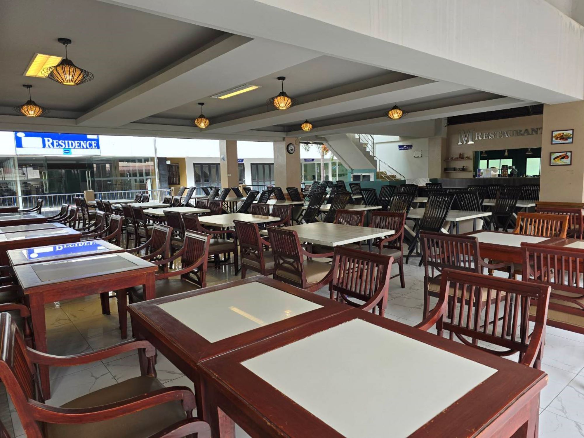 A dining area with multiple tables and chairs, a sign for 'RESIDENCE' in the background, and a restaurant sign above the seating area.