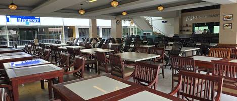 A dining area with multiple tables and chairs, a sign for 'RESIDENCE' in the background, and a restaurant sign above the seating area.
