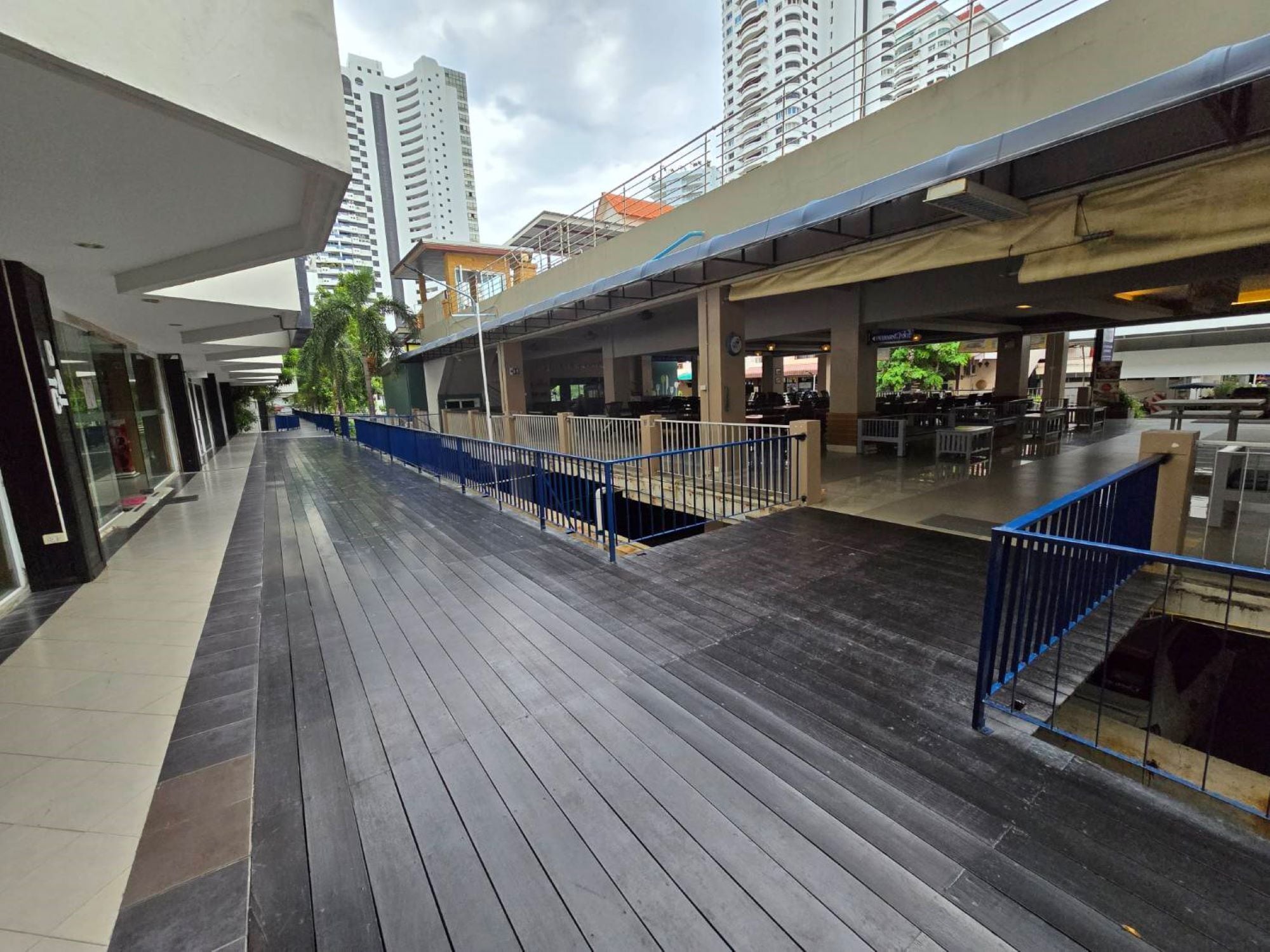 A covered outdoor walkway with a blue railing, connecting various buildings and shops.