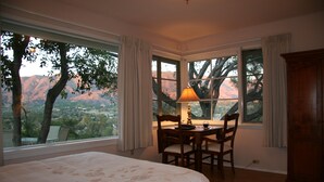 A bedroom with a large bed, a desk with chairs, and a view of mountains through the windows. - Ojai Retreat & Inn (Ojai)