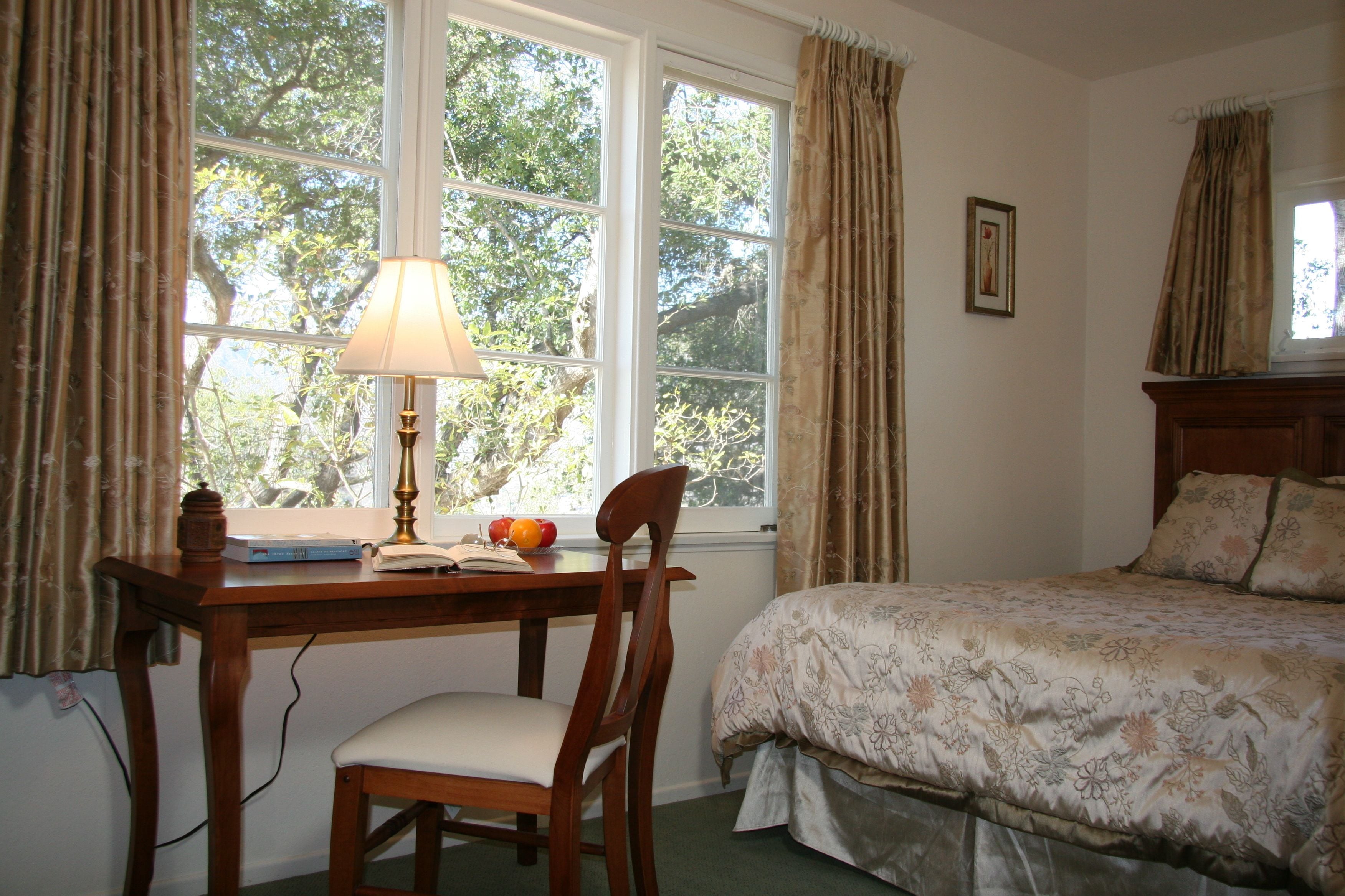 A bedroom with a bed, a desk with a lamp, and a chair.