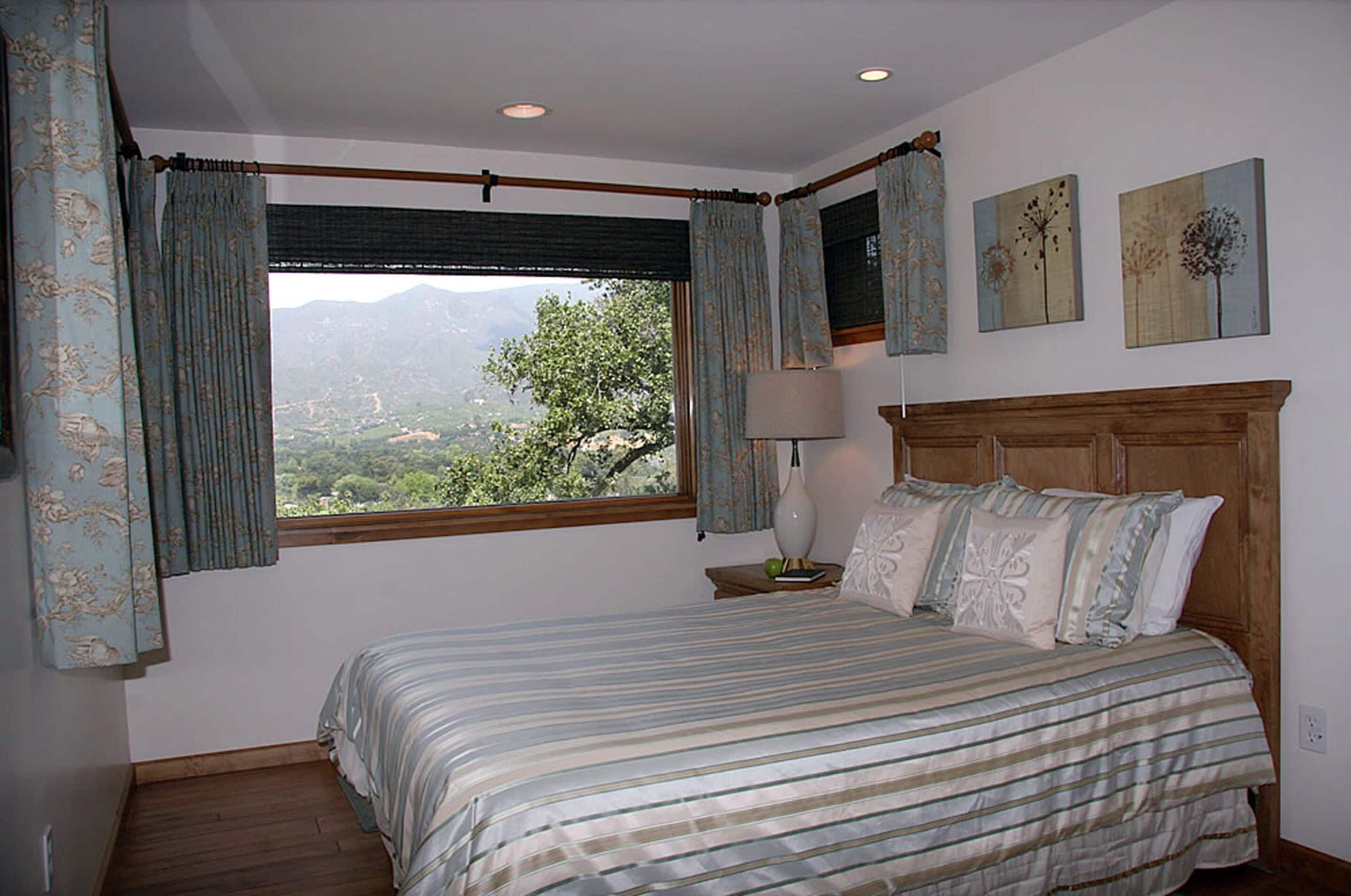 Un dormitorio con cama, cortinas, mesita de noche, lámpara y decoración en la pared.
