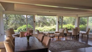 A spacious dining area with a large table and multiple chairs, large windows offering a view of greenery, and a patterned rug on the floor. - Ojai Retreat & Inn (Ojai)