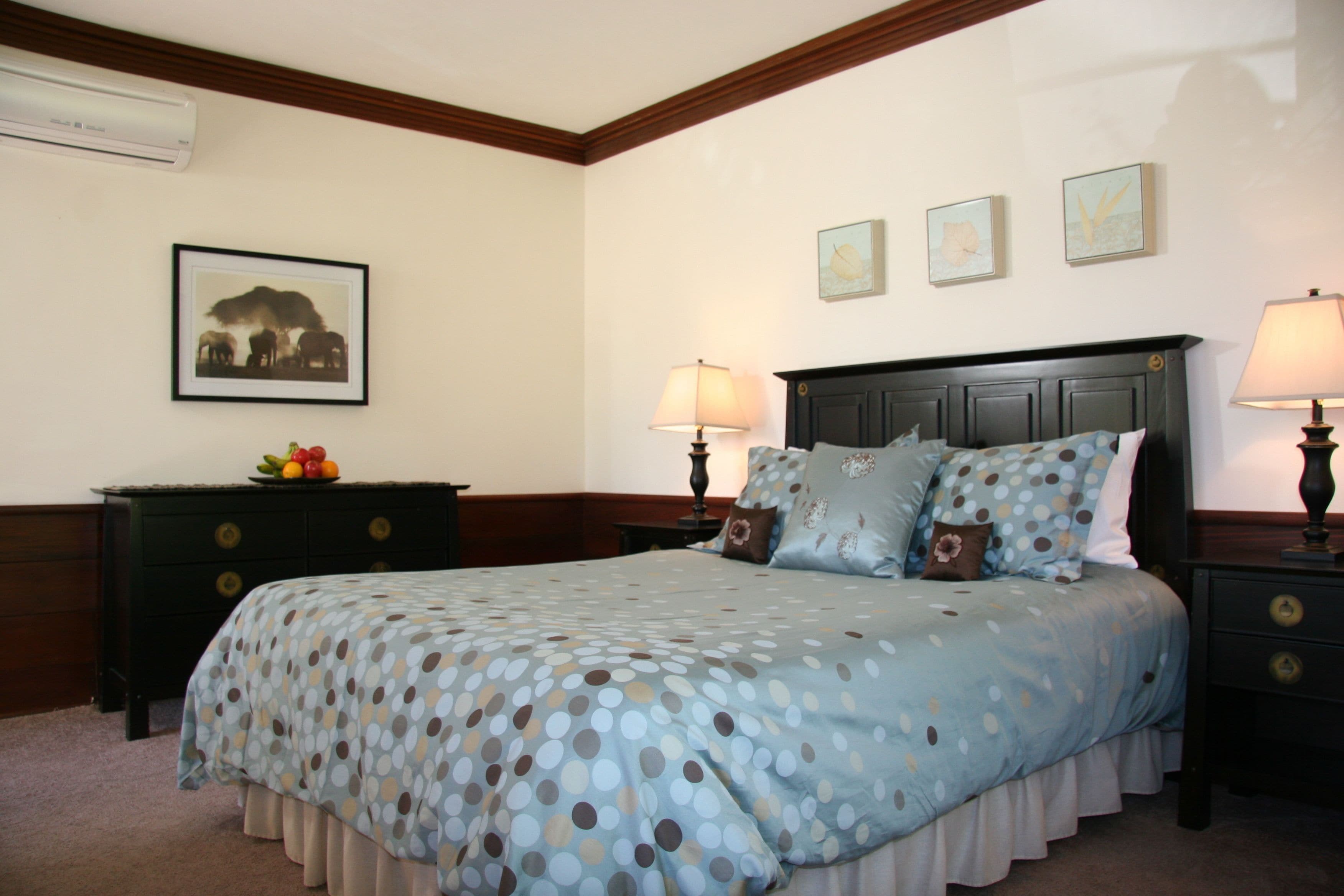 A neatly arranged bedroom with a bed, two bedside tables, a dresser, and a wall-mounted air conditioner.