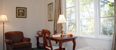 Una habitación con cama, una silla de madera, una mesita con lámpara y una ventana con cortinas.