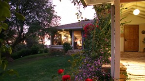 A house with a covered porch, a stone pathway leading to the door, and a well-maintained lawn with flowering plants. - Ojai Retreat & Inn (Ojai)