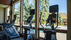 A gym with treadmills and exercise bikes, large windows, and a view of trees and a pool. - Terracehouse - CoralTree Residence Collection (Snowmass Village)